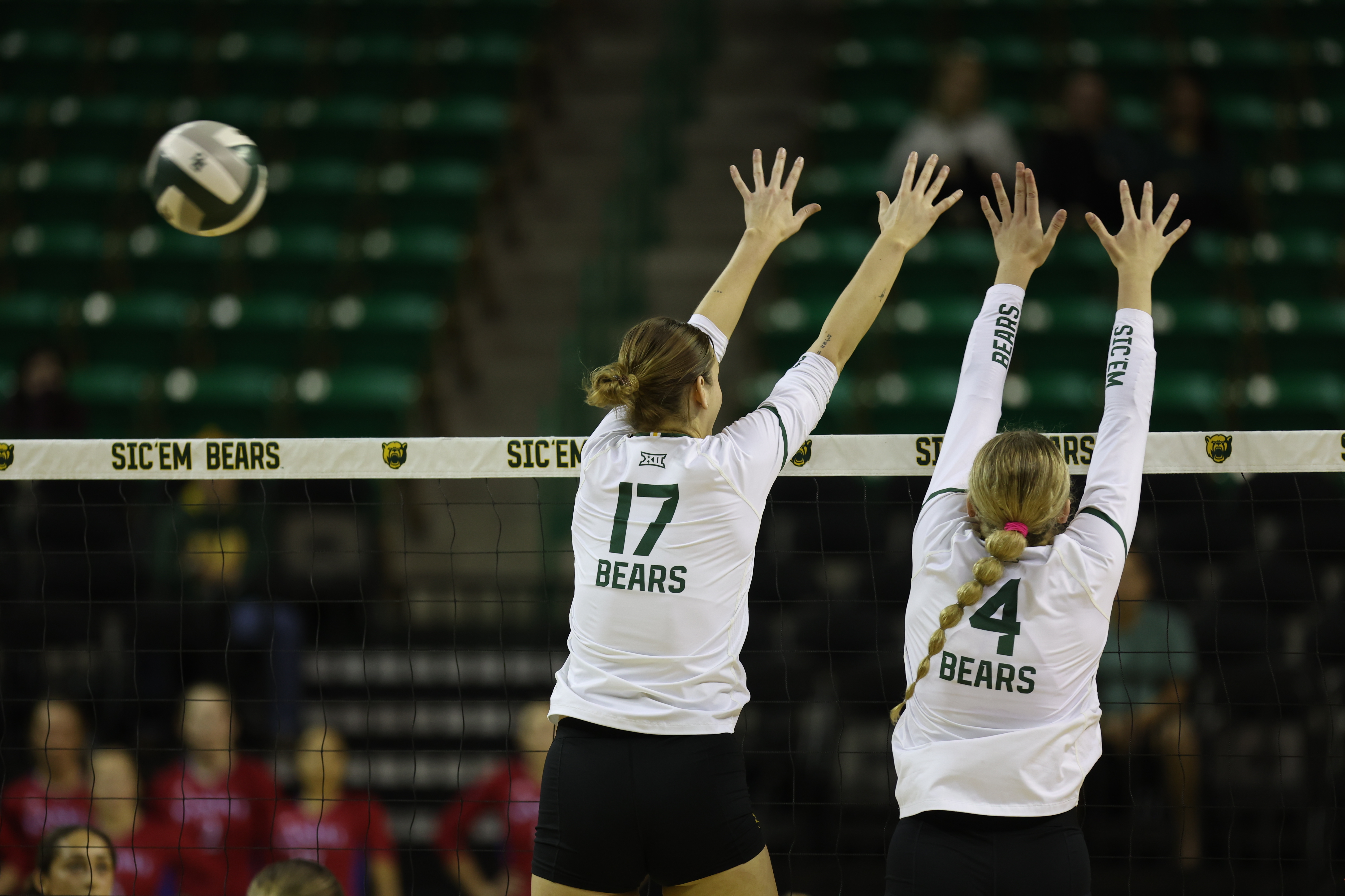 Two players from Baylor Womens Volleyball jumping at the net with the ball next to them in the air. 