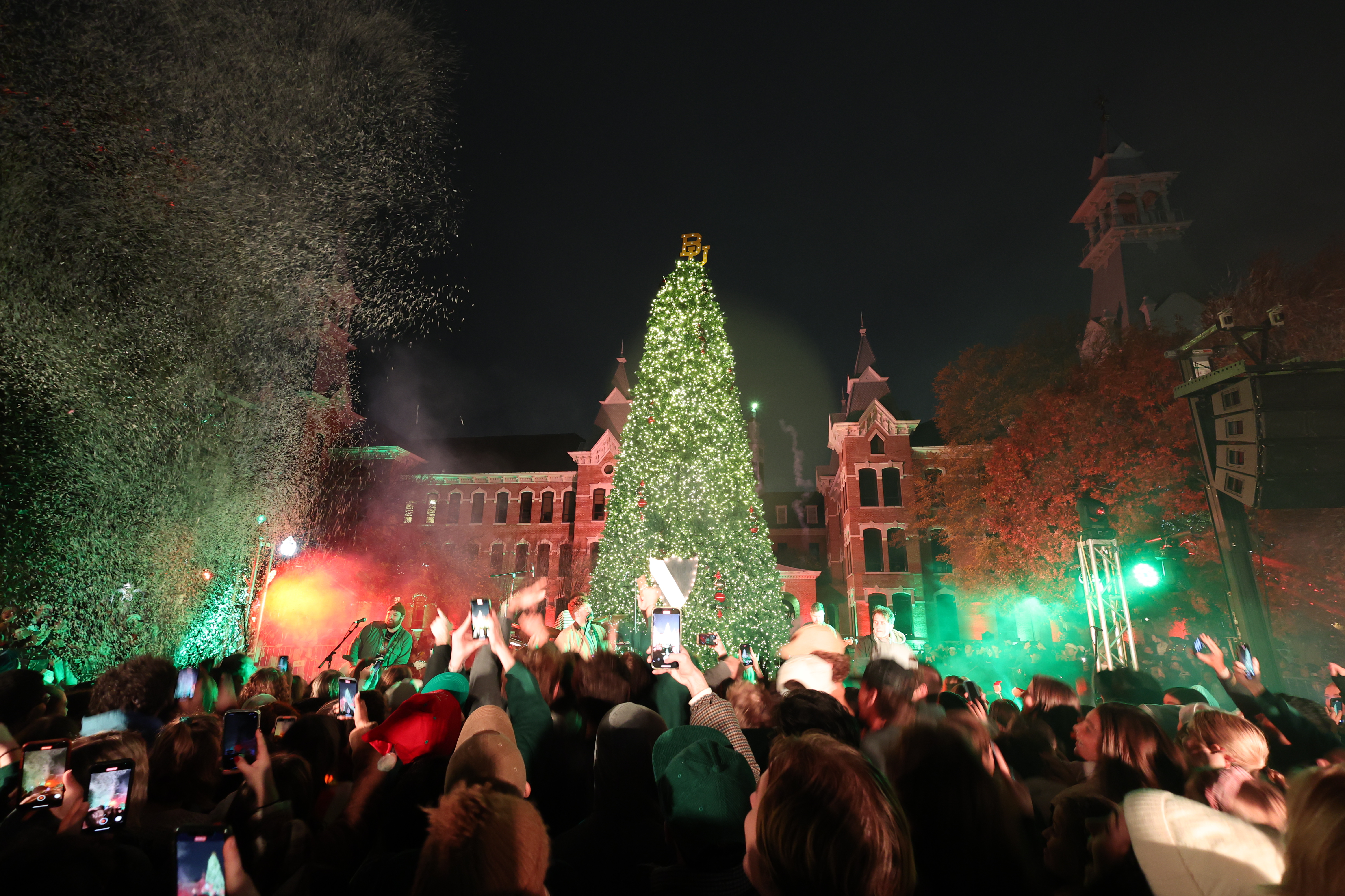 A large crowd dances in green and red lights before a large Christmas tree with the Baylor University symbol atop the tree.