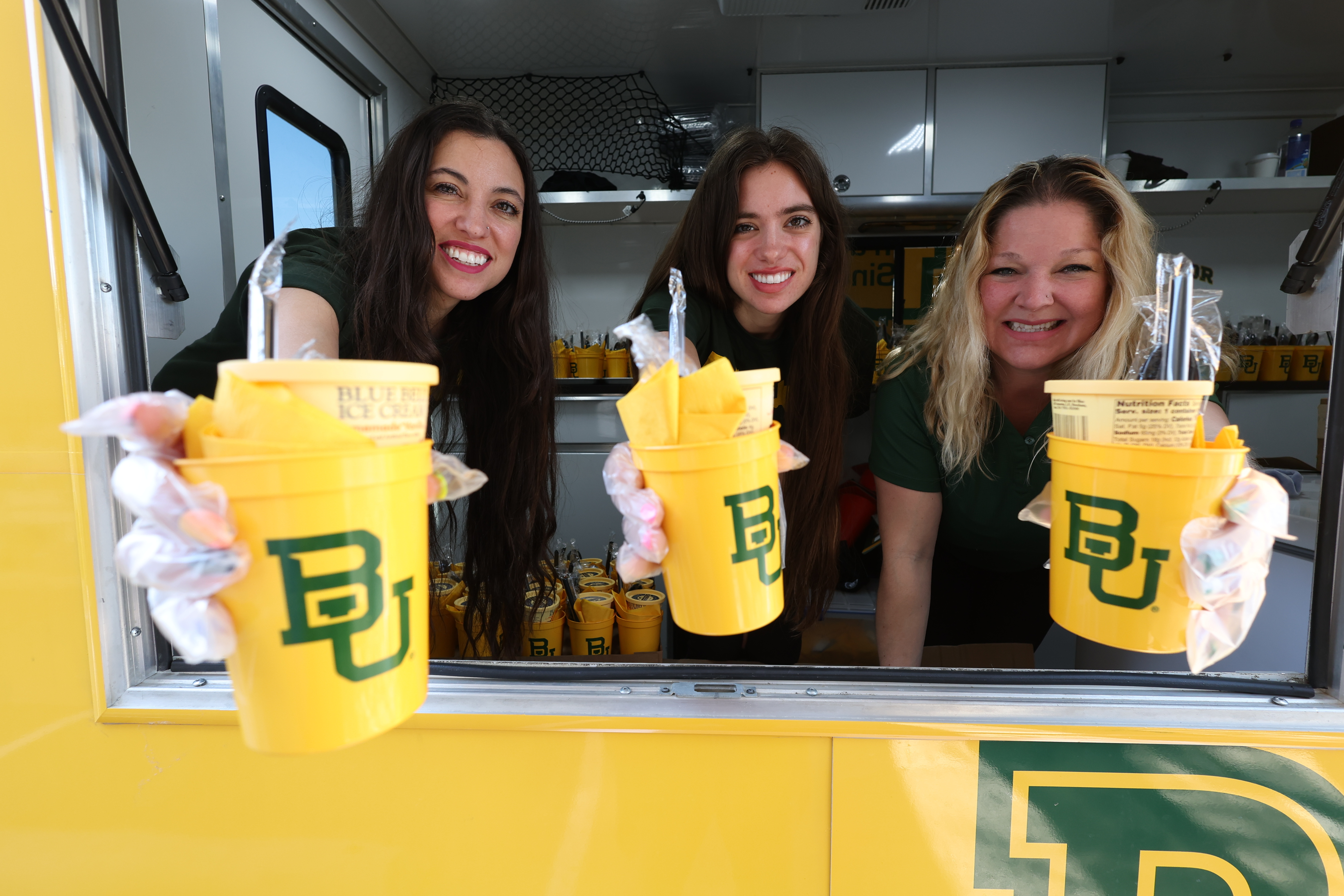 Three smiling women hold out Dr Pepper floats from outside the window of a food truck. 