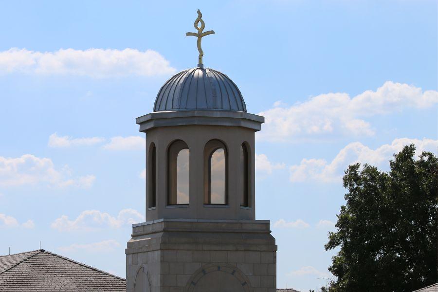 Photo of the clock tower cross set against a blue sky.