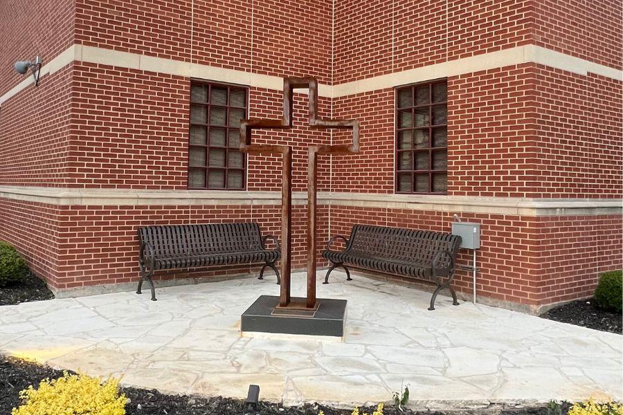 Photo of the empty cross against a brick wall setting.